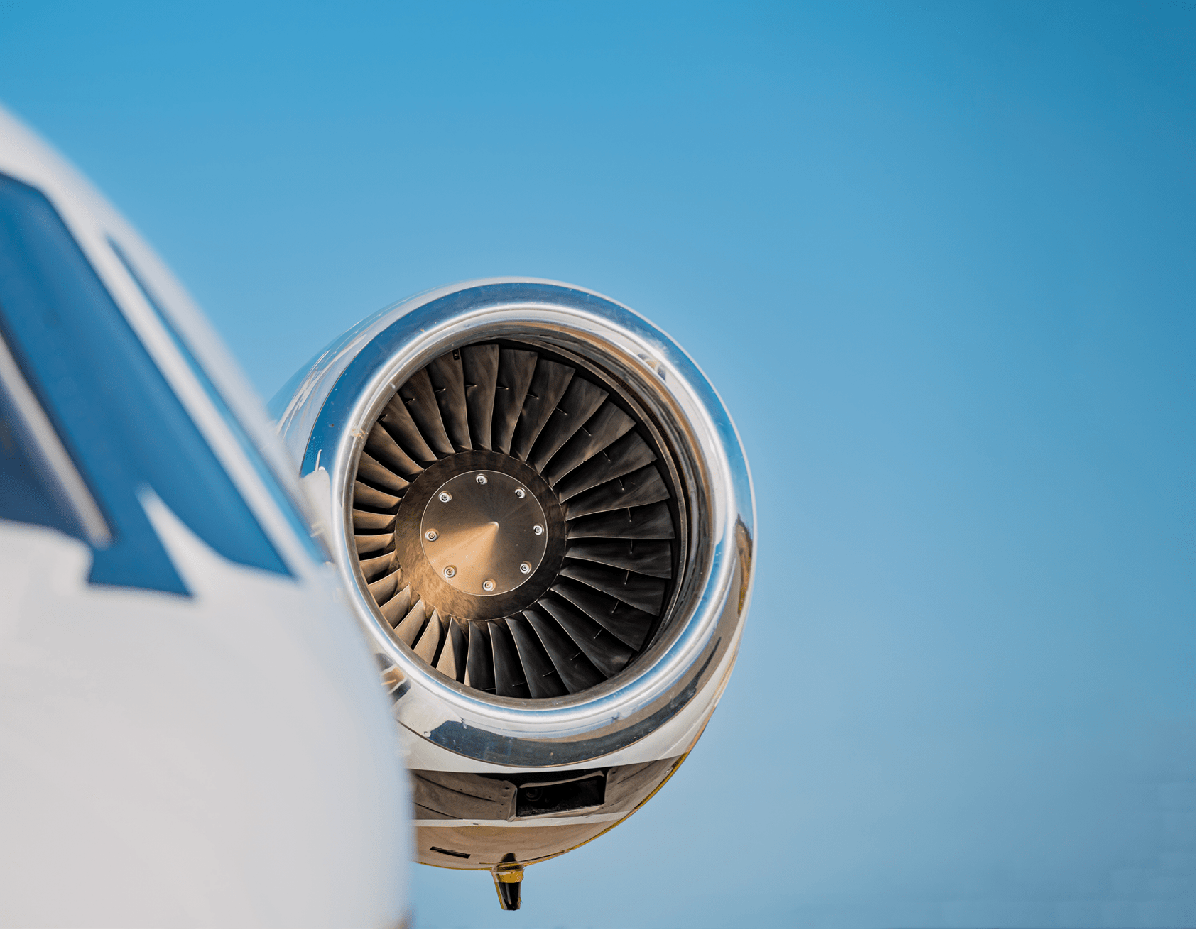 High mounted jet engine in focus with the cockpit and fuselage in soft focus. A clear blue sky frames the jet engine.
